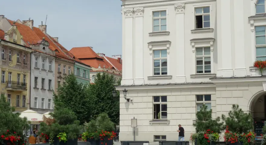 Urokliwe miasto nad Prosną z zabytkową architekturą, zielenią i ławkami w centrum.