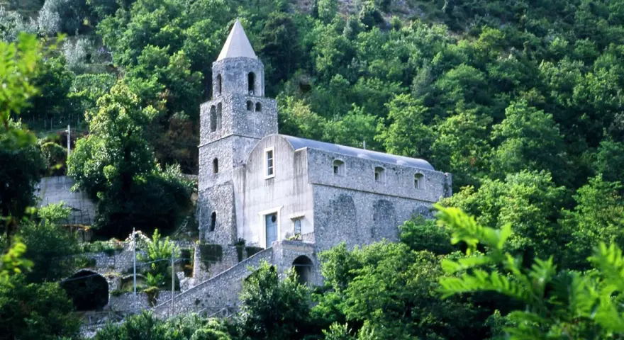 Antica chiesa in pietra su un fianco di montagna, circondata da alberi lussureggianti. I tramonti montagna qui sono magici.