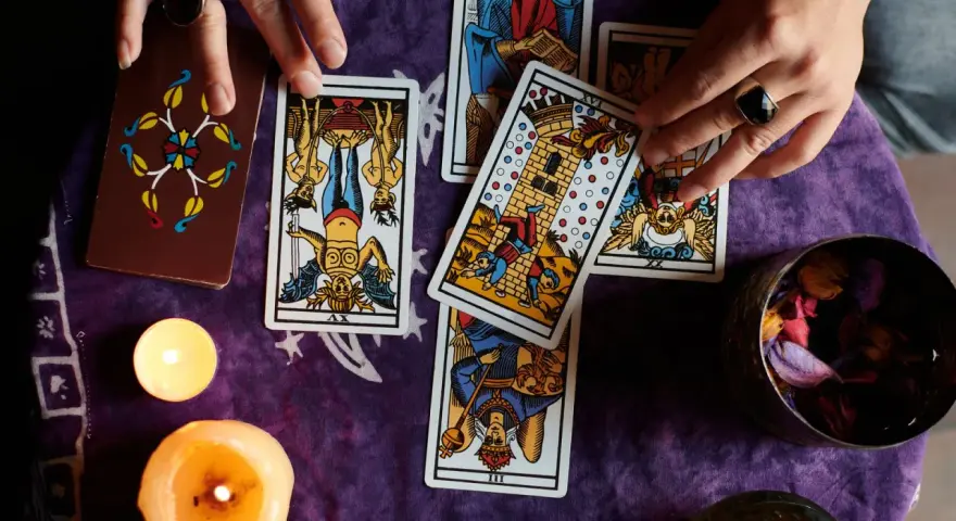 Manos de tarotista que es, barajando cartas y velas encendidas sobre tela morada.
