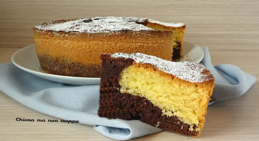 Una fetta di torta da colazione morbidissima bicolore, al cacao e vaniglia, cosparsa di zucchero a velo.