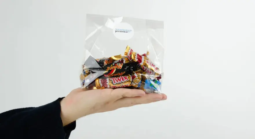 En hand håller en presentkorg i cellofan fylld med choklad.