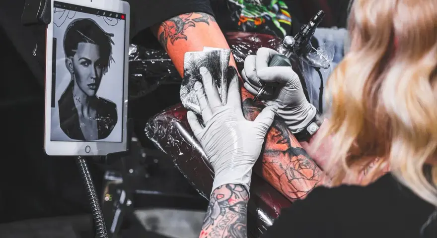Artysta wykonuje tatuaż twarzy, używając szarego mydła do mycia tatuażu. Na tablecie widnieje wzór.