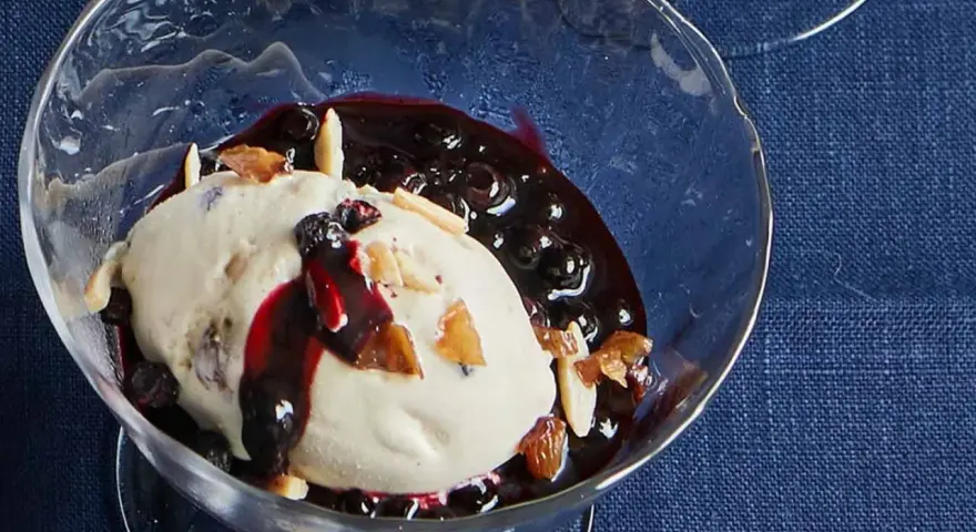 Cremiges Malaga Eis Rezept mit Blaubeersauce und Mandelsplittern in einer Glasschale.
