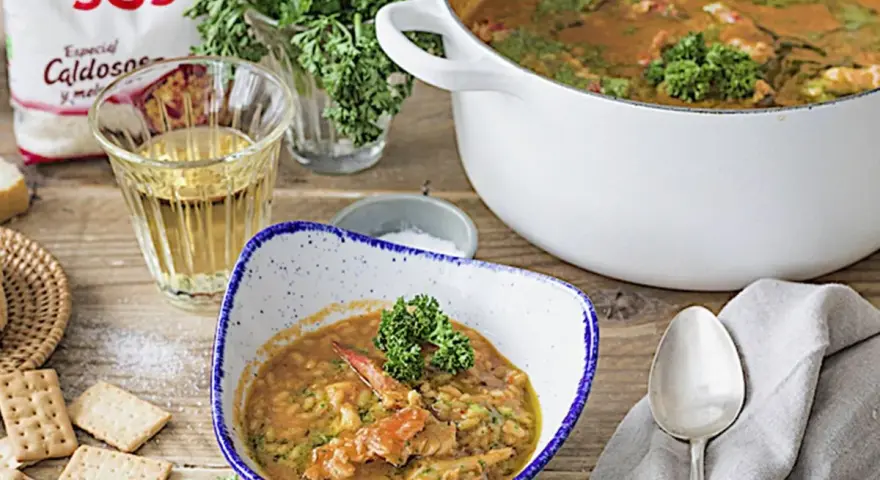 Delicioso arroz con bogavante servido en un cuenco, con una cazuela llena y una bolsa de arroz SOS al fondo.