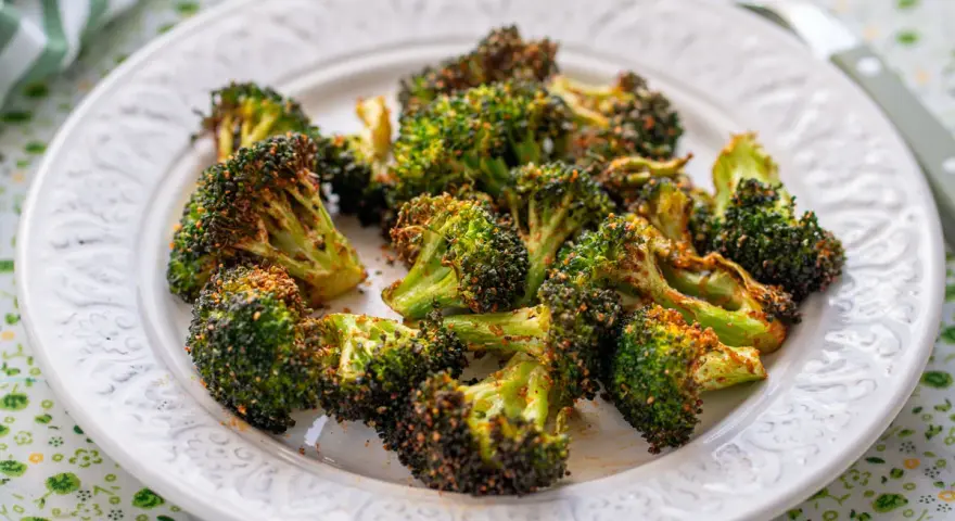 Brocoli en airfryer, crujiente y dorado, servido en un plato blanco con un mantel verde.