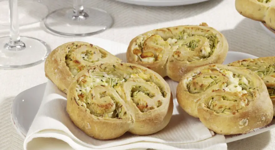 Zucchini Schnecken mit Käsefüllung auf einem Teller mit weißer Serviette.