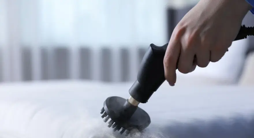Main d'une personne utilisant un nettoyeur vapeur pour nettoyer un matelas en mousse. Une méthode efficace pour savoir comment nettoyer un matelas en mousse.