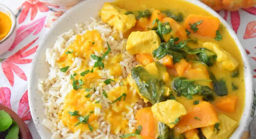 Aromatyczny kurczak curry z dynią i mlekiem kokosowym, podany z ryżem i posypany natką pietruszki.
