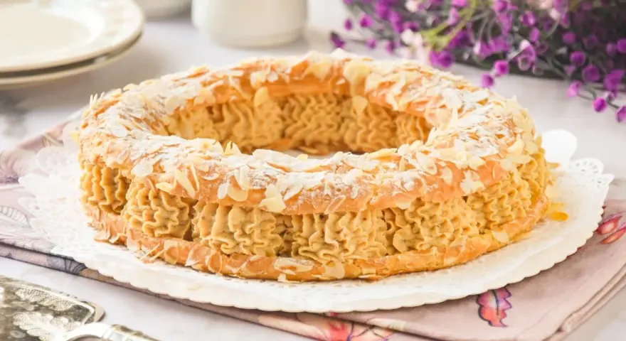 Un delicioso praliné que es un pastel Paris-Brest, cubierto de almendras laminadas y espolvoreado con azúcar glas.