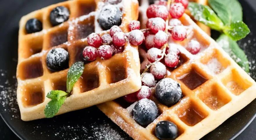 Keto gofry z mąki kokosowej z borówkami, porzeczkami i miętą, posypane cukrem pudrem.