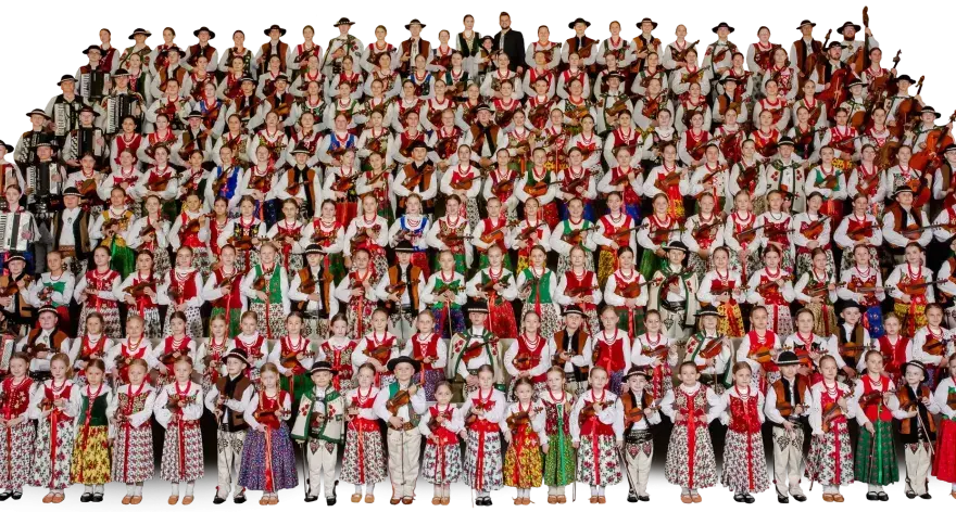 Wielka grupa dzieci i młodzieży w strojach ludowych, grających na akordeonach i skrzypcach. To piękna prezentacja muzyki ludowej Mazowsza.