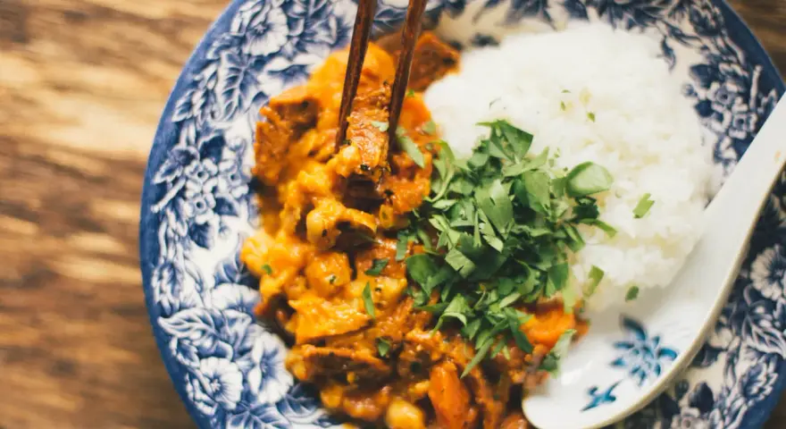 Miseczka z ryżem i curry, podana z posiekaną natką pietruszki, jedzona pałeczkami.