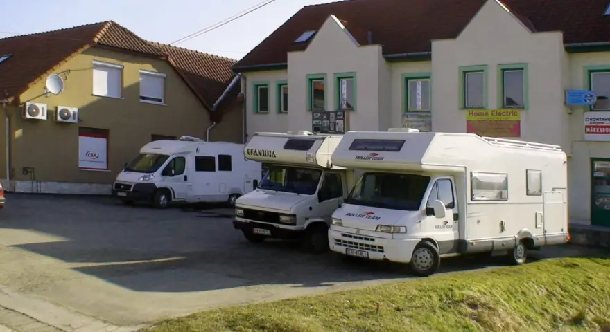 Trzy białe kampery zaparkowane przed budynkami z szyldami.