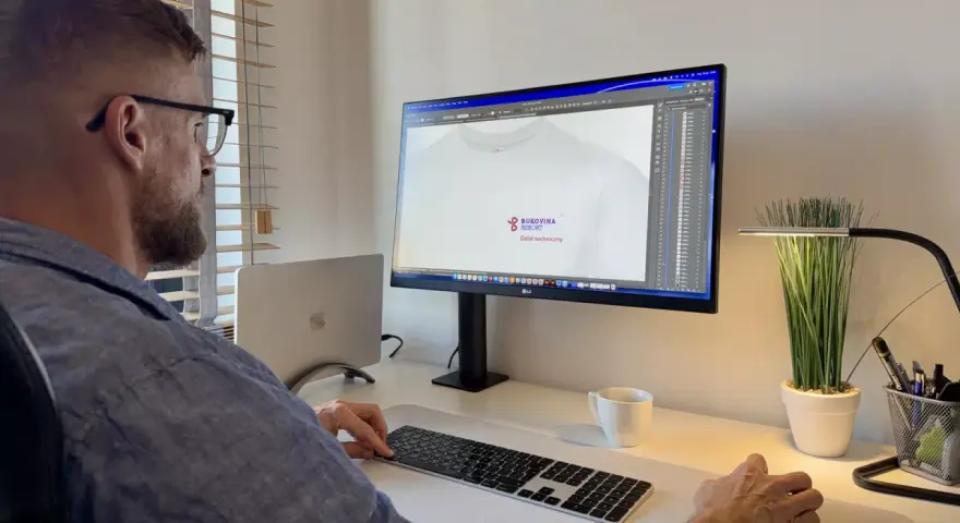 Mężczyzna pracuje przy komputerze, projektując logo na koszulkę. Pokazuje, jak napisać tekst na komputerze i go wydrukować.