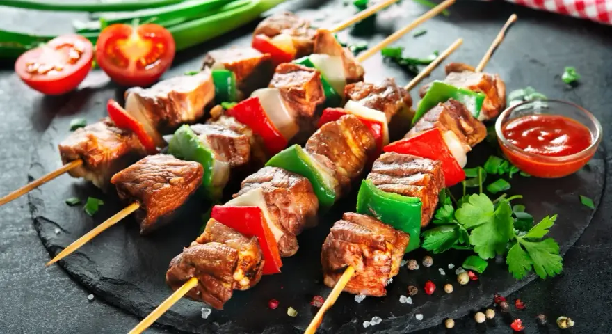Spiedini di carne succulenti con peperoni e cipolle, pronti per essere gustati con una salsa rossa e pomodorini freschi.