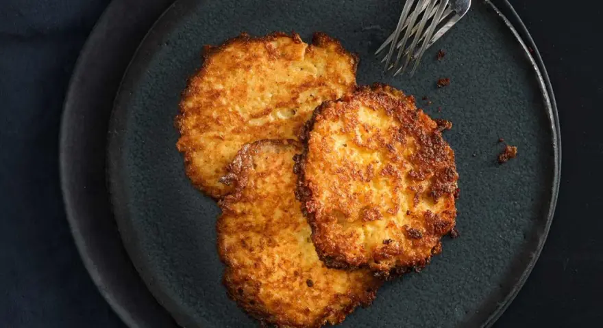 Drei goldbraune Kartoffelpuffer, frisch zubereitet im Thermomix, liegen auf einem dunklen Teller.