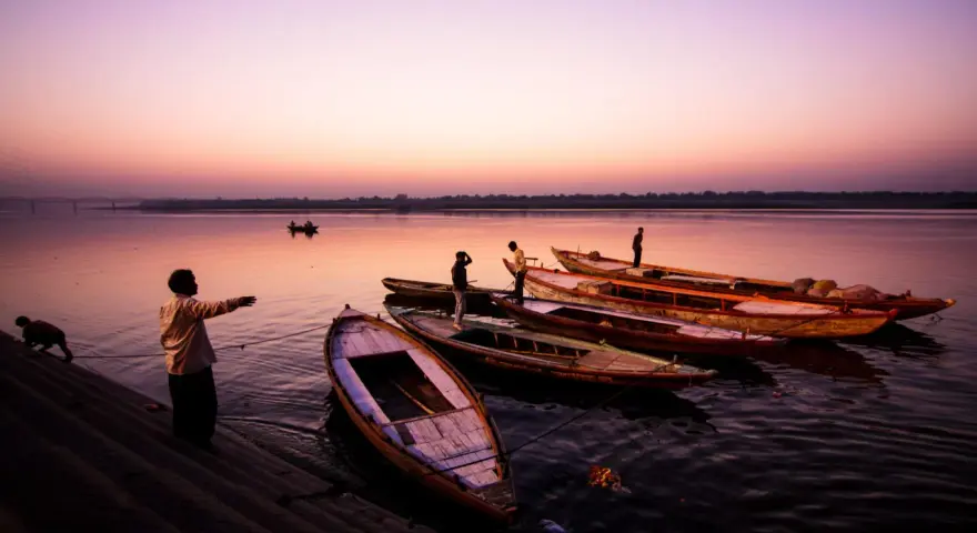 Vue d'ensemble de bateaux amarrés sur un fleuve au crépuscule, avec des silhouettes humaines sur la rive. Ces photos grand angle capturent la sérénité du moment.