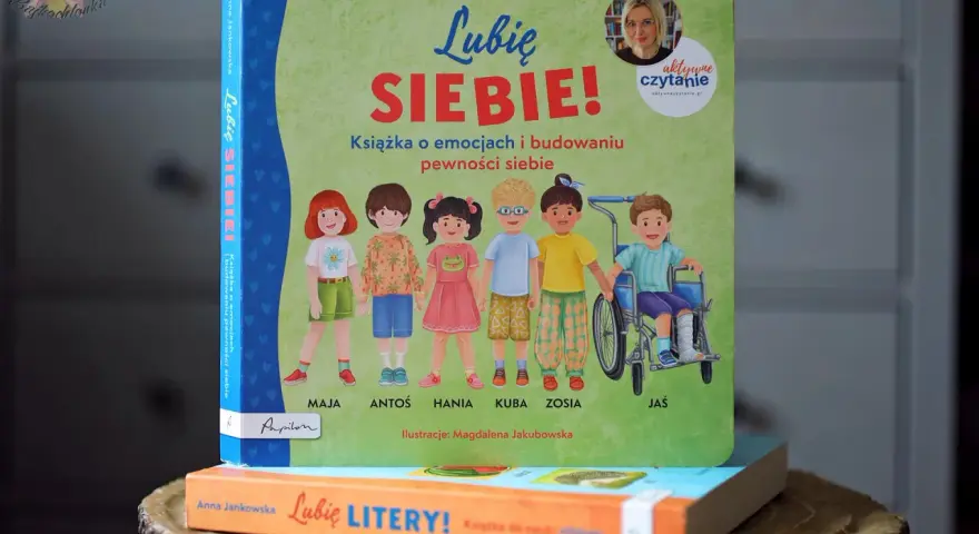 Książka "Lubię SIEBIE!" Anny Jankowskiej to pomoc w budowaniu pewności siebie u dzieci. Ilustracje przedstawiają grupę uśmiechniętych dzieci, w tym chłopca na wózku.
