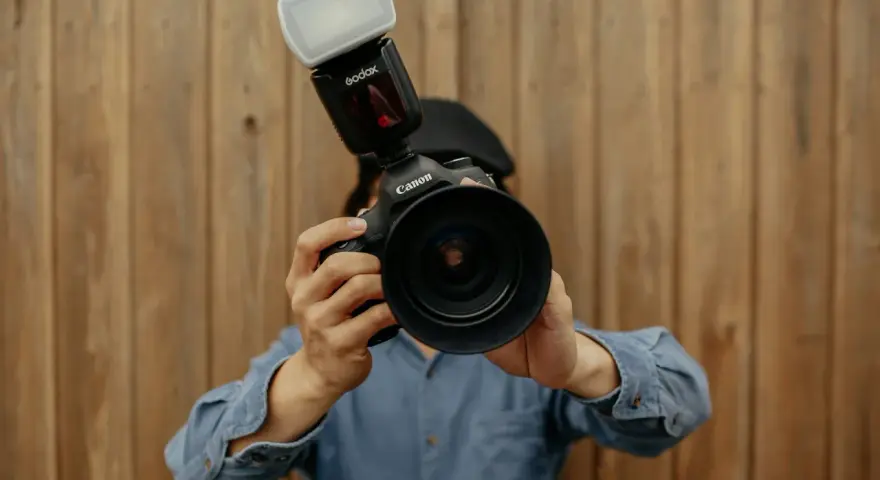 Fotograf trzyma aparat Canon z lampą błyskową. Liczba przewodnia lampy błyskowej jest kluczowa dla uzyskania idealnego oświetlenia.
