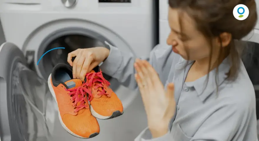 Donna con scarpe arancioni davanti a una lavatrice. Scopri come fare un lavaggio a vuoto per pulire la lavatrice.