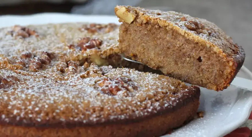 Une part est soulevée d'un délicieux gâteau aux noix, saupoudré de sucre glace.