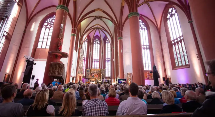 Menschen sitzen in einer Kirche, die für eine Veranstaltung beleuchtet ist. Es ist schön, dass man wieder in die Kirche eintreten kann.