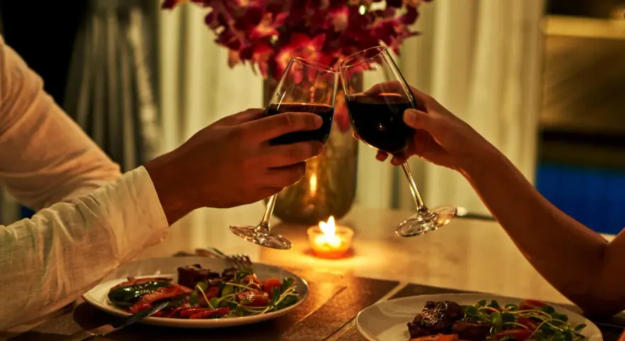 Para wznosząca toast kieliszkami z czerwonym winem podczas romantycznej kolacji przy świecach.