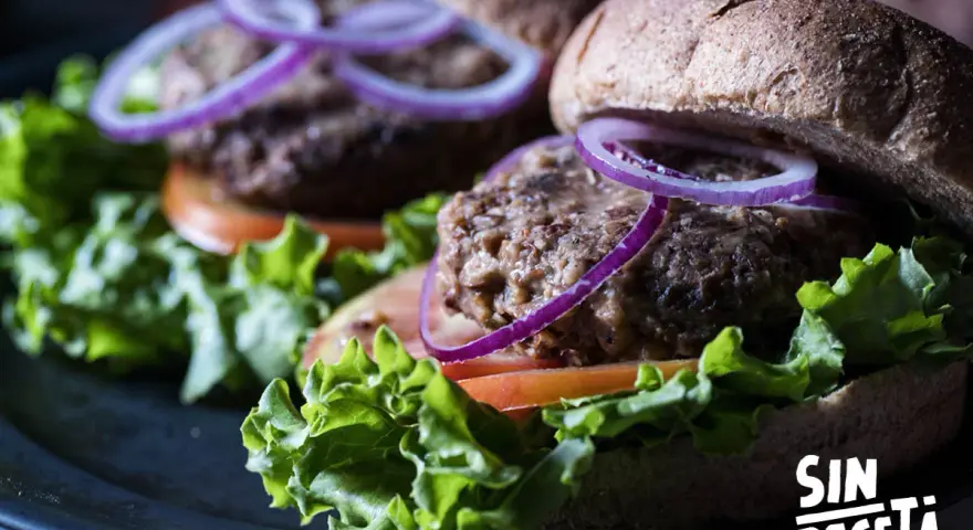 Dos deliciosas hamburguesas de lentejas con lechuga fresca, tomate y aros de cebolla morada, listas para disfrutar.