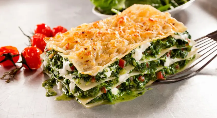 Deliciosa lasaña de verduras, con capas de pasta, espinacas y queso cremoso, acompañada de tomates cherry.