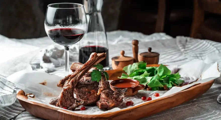 Saftige Lammkoteletts mit frischem Salat und einem Glas Rotwein. Die perfekte Wahl, welcher Wein zu Lamm passt, ist oft ein kräftiger Rotwein.