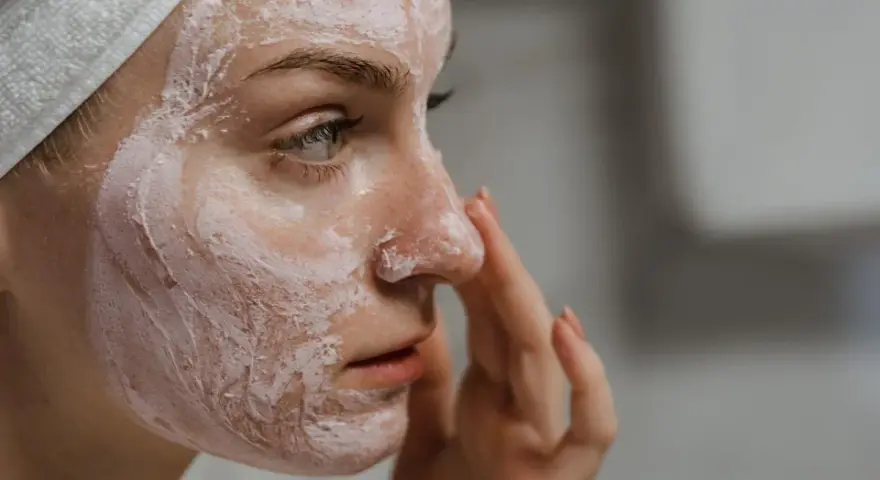 Mujer con mascarilla rosa en la cara, aprendiendo como exfoliar la cara para una piel radiante.