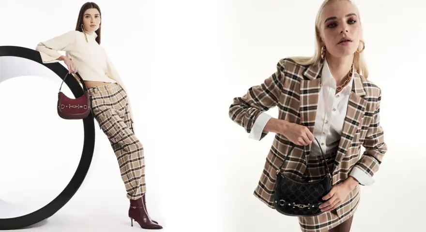 Due modelli mostrano idee outfit ufficio inverno: uno con maglione a collo alto, pantaloni a quadri e borsa bordeaux; l'altro con blazer a quadri, camicia bianca e borsa nera.