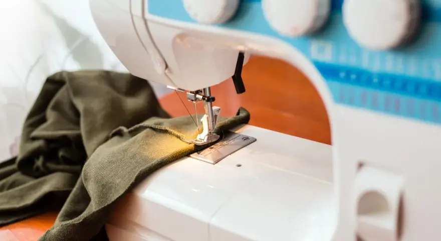 Maszyna do szycia z zieloną tkaniną. Zastanawiasz się, dlaczego maszyna do szycia zrywa górną nitkę? Może problem tkwi w igle lub naprężeniu?