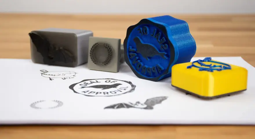 A blue 3d print stamp with a seal of approval design sits next to a yellow one.
