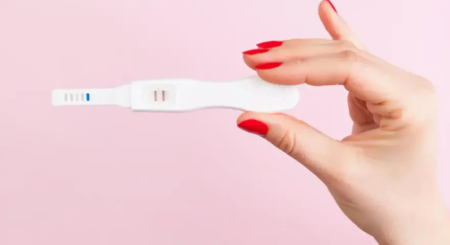 Dłoń z czerwonymi paznokciami trzyma test ciążowy z dwoma kreskami. To może być sygnał, że doszło do ciąży biochemicznej.