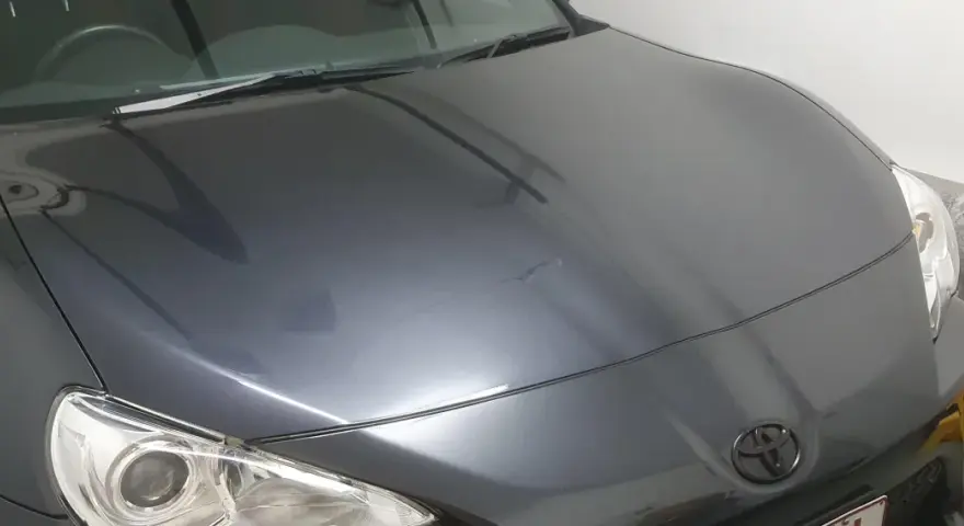 A dark grey car hood with a Toyota emblem. The paint has some minor imperfections, hinting at the question: how long does it take to clay bar a car?