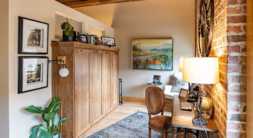 Accogliente angolo studio con un armadio a scomparsa in legno, un tappeto persiano e un quadro paesaggistico, che evoca l'atmosfera di una piccola casa di campagna.