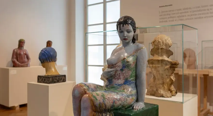 Ceramiczna rzeźba kobiety w kwiecistej sukni, dzieło inspirowane twórczością Olgi Niewskiej, prezentowana w muzeum.