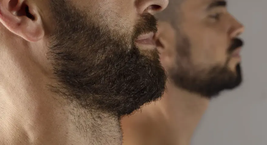 Primer plano de un hombre con barba oscura y tupida, reflejado en un espejo. La imagen captura la decisión de dejar crecer la barba.