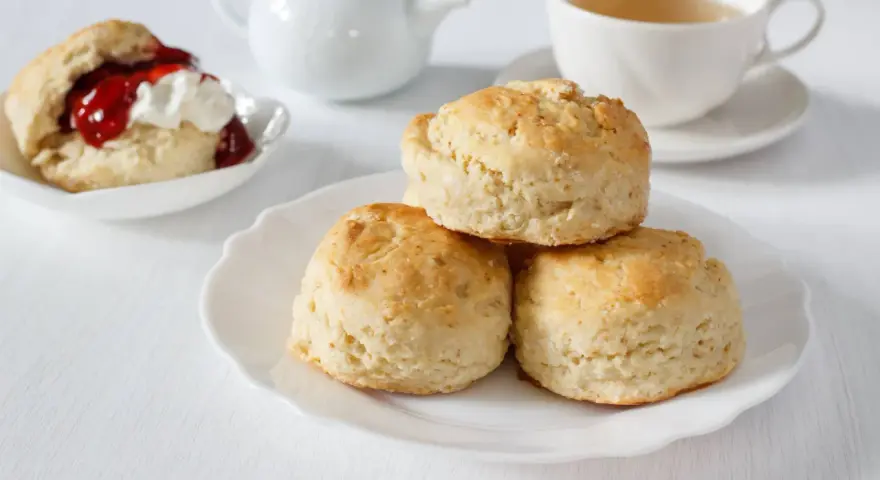 Goldbraune Scones, ein Klassiker zum Tee. Sie sind kleine, süße Gebäckstücke, die oft mit Marmelade und Sahne serviert werden.
