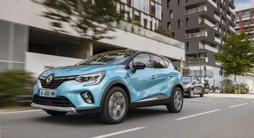Un Renault Captur azul circula por una ciudad moderna. Es un híbrido no enchufable, eficiente y elegante.
