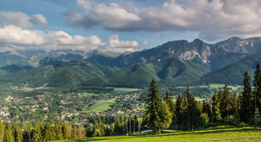 Widok na Tatry z Zakopanem u podnóża. W oddali widać skaliste szczyty, a bliżej zielone zbocza porośnięte lasem. To właśnie takie krajobrazy tworzą regle.
