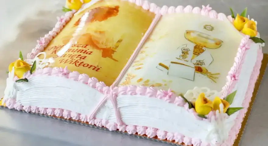 Eleganckie ciasto na komunię w kształcie otwartej księgi z motywami religijnymi i napisem "Pierwsza Komunia Święta Wiktorii".