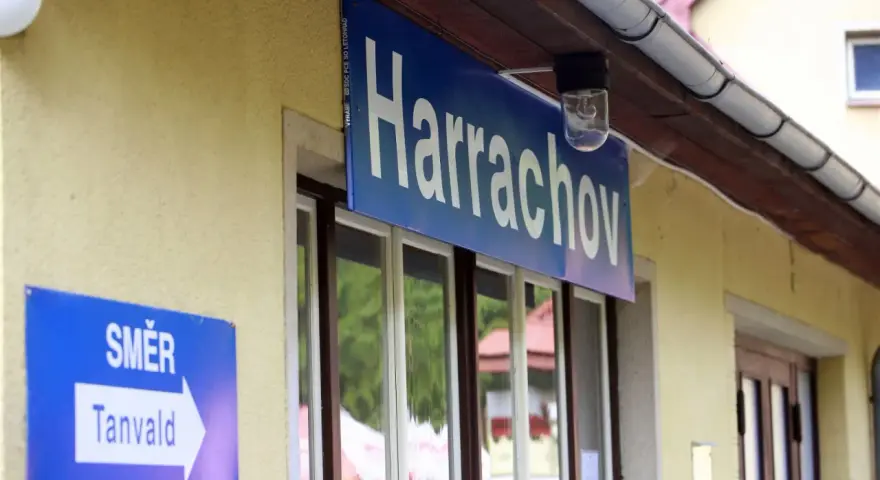 Tabliczka "Harrachov" nad oknami dworca. Obok znak kierunkowy "Směr Tanvald". Pociąg Szklarska Poręba Harrachov czeka na pasażerów.