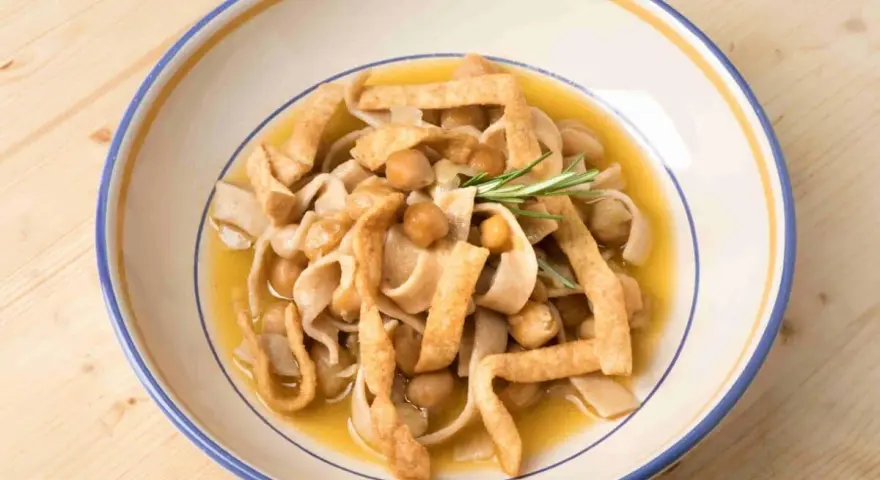 Un piatto di ciceri e tria, pasta fresca con ceci e sfoglie fritte, guarnito con rosmarino.