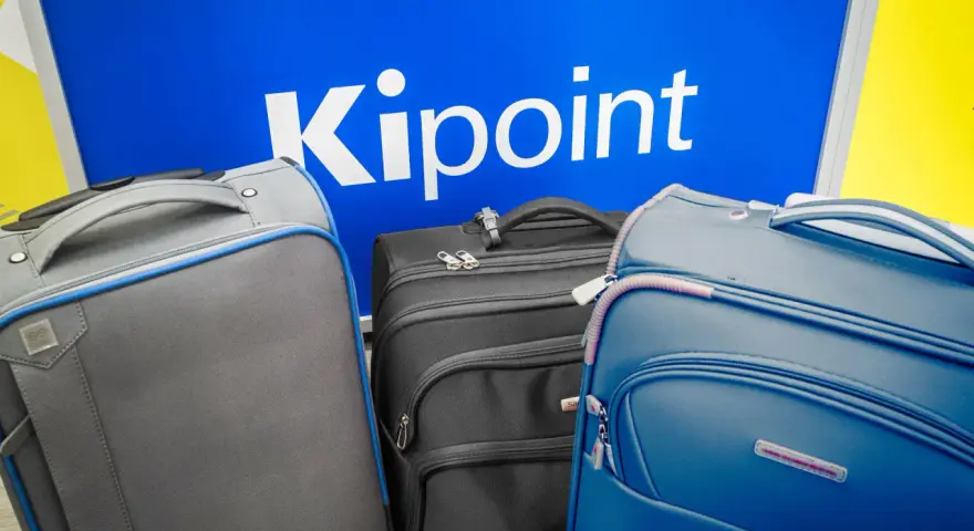 Three suitcases in front of a blue sign with "Kipoint" in white letters.