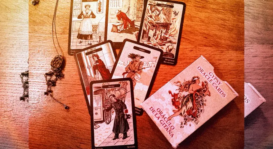 Rozłożone karty cygańskie, w tym "Służąca", "Żołnierz" i "Nieszczęście", obok pudełka "Gypsy Oracle Cards".