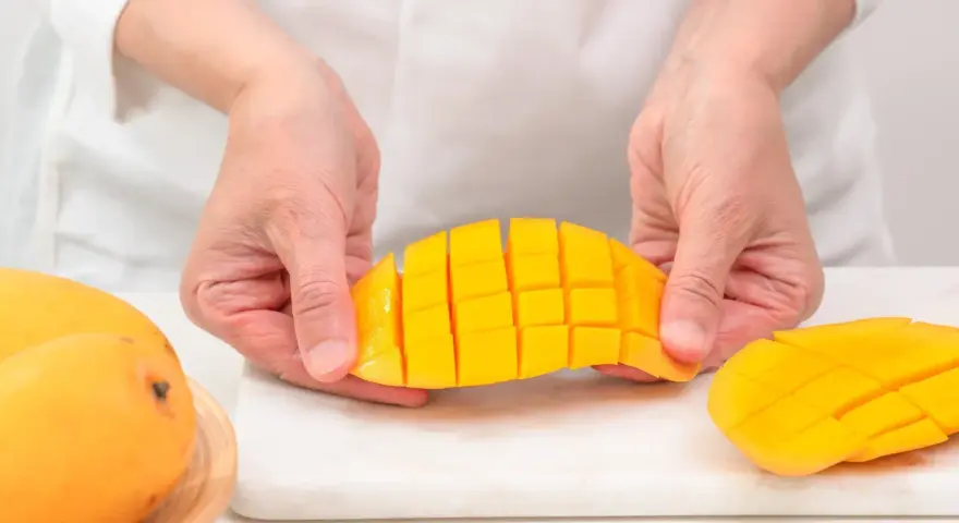 Ręce kroją dojrzałe mango na kostki. Czy mango ma pestkę? Tak, ale jej nie widać, bo jest w środku.