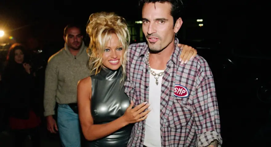 Pamela Anderson i Tommy Lee, ikony lat 90., pozują do zdjęć. Pamela w błyszczącej sukience, Tommy w kratowanej koszuli.
