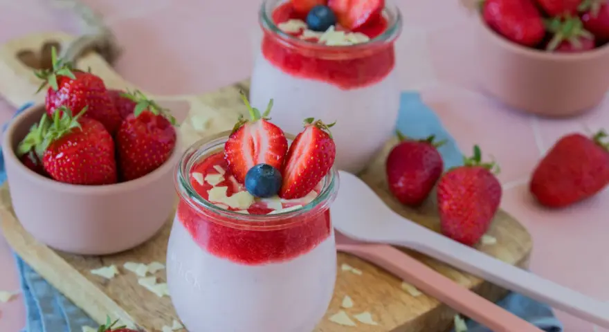 Zwei Gläser mit cremigem Joghurt und Erdbeersoße, garniert mit frischen Erdbeeren und Blaubeeren. Ein schneller Nachtisch mit Erdbeeren, der Lust auf mehr macht.